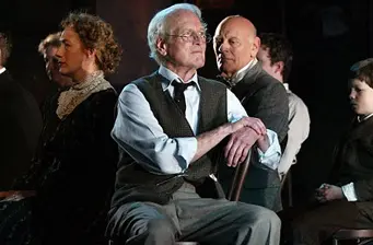 Paul Newman sitting with others in vintage formal clothes, arms crossed