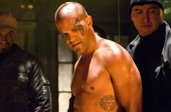 shirtless man with face tattoo stands tense between two men