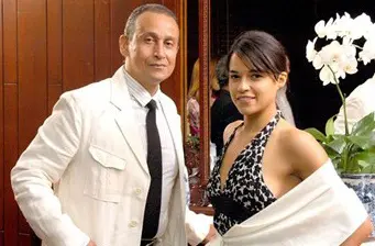 Man in white suit and woman in black and white dress pose indoors