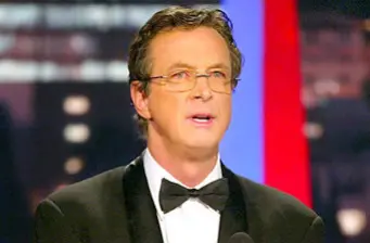 Michael Crichton in tuxedo speaking at an indoor event