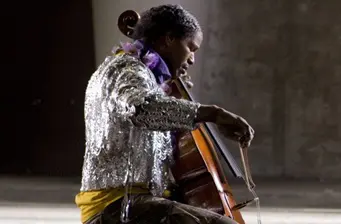 man in silver jacket playing cello indoors