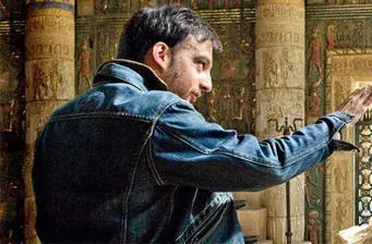 Man in denim jacket reaches out inside historic columned space