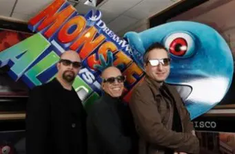 Three men stand before large Monsters vs. Aliens sign