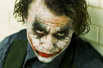 Joker character in smeared white and black makeup looks up intensely