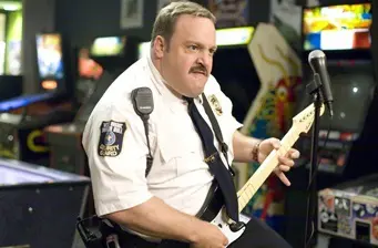 Paul Blart in mall cop uniform playing electric guitar indoors