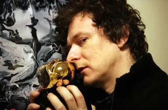 Michel Gondry inspects small gold figurine in close-up