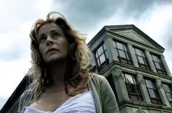 Woman in white top looks up beside old multi-windowed building
