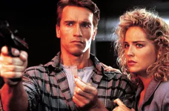 Arnold Schwarzenegger aims gun, Sharon Stone watches closely in scene