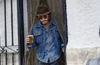 Man in brown hat and denim jacket holding beer at doorway