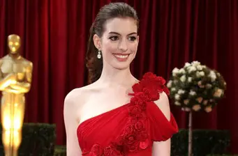 Anne Hathaway in red dress at event with statue and flowers behind