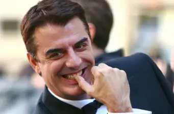Chris Noth smiling with hand near mouth in casual moment
