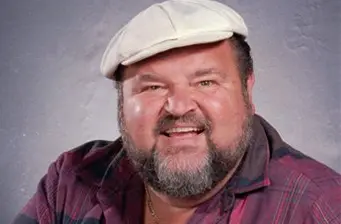 Dom DeLuise smiling in cap and plaid shirt headshot