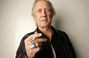 David Carradine in black jacket showing multiple rings on fingers