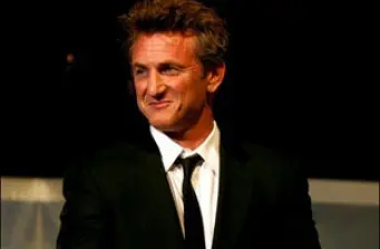 Sean Penn in black suit and tie with smirking expression