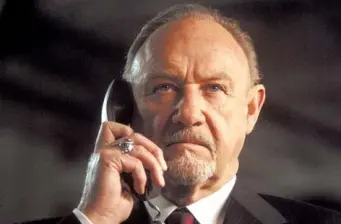 Gene Hackman holds phone, serious expression in close-up movie still