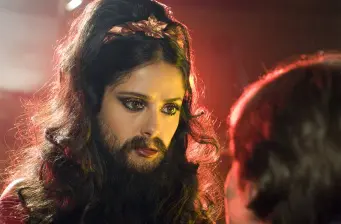 Person with dark hair and beard makeup in dramatic lighting
