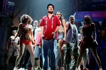 group of diverse performers in streetwear on stage, one in red shirt center