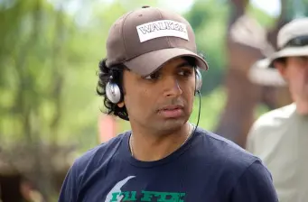 M. Night Shyamalan wearing headphones and a cap outdoors