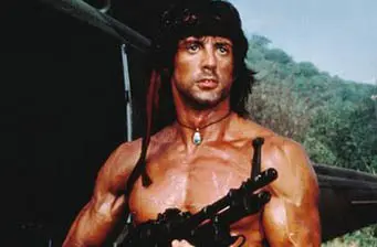 Sylvester Stallone shirtless as Rambo holding machine gun outdoors