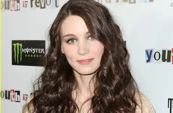 Woman with long brown hair poses at event with Monster Energy logo behind