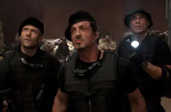 Three men in tactical gear standing alert in dark interior scene