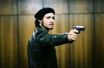 man in leather jacket aiming pistol indoors, tense expression