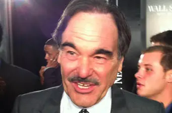 Oliver Stone close-up smiling at an event with people blurred behind