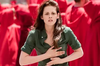 Woman in green shirt clutching chest with red-robed people behind