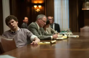 Men seated around a table in a meeting, one looks away
