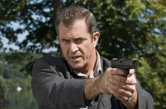 Mel Gibson aims pistol with intense expression outdoors