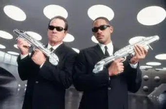 Two Men in Black agents in suits holding silver futuristic guns indoors