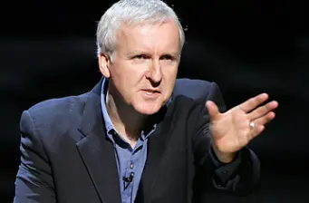 Man in dark blazer speaking and gesturing with hand forward