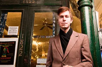 Man in brown suit jacket stands outside building entrance