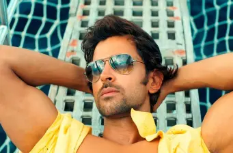 Man in sunglasses reclines in hammock with yellow shirt open