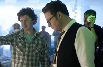 two men, one points, one looks down, film set background
