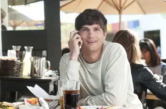 young man talking on phone at outdoor cafe table with drink