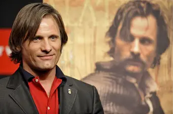 Viggo Mortensen in suit with movie poster blurred behind him