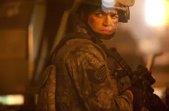 Michelle Rodriguez in military uniform holding a gun looking back