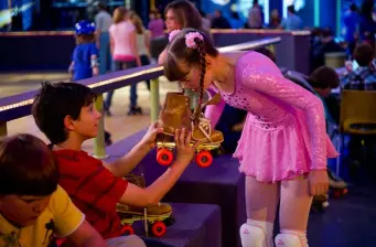 Boy handing roller skates to girl in pink dress at indoor rink