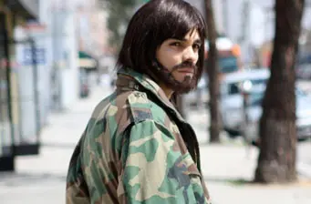 a man in camouflage jacket stands on city street looking sideways