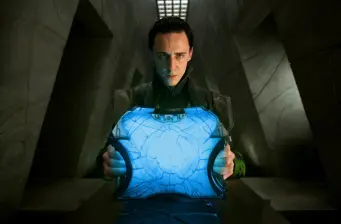Loki gripping the glowing blue Tesseract in a dark setting