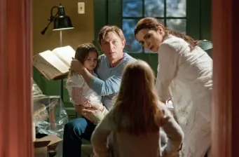 Man holds young girl while woman and another child watch inside house