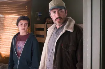 two men indoors, one with cap and jacket, other in hoodie