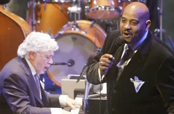 Male pianist and singer perform on stage with drum set behind