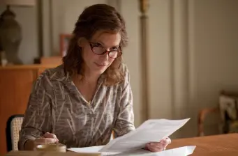 Sandra Bullock seated at table reading paper indoors