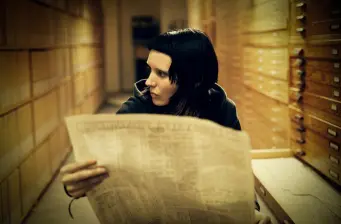 Woman with black hair reading newspaper in hallway lined with drawers