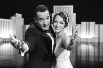 Two actors from The Artist reach forward smiling in black and white