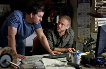 Two men study a map closely over a cluttered desk in an office