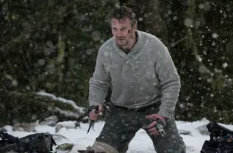 Man crouches in snow holding two knives during a storm