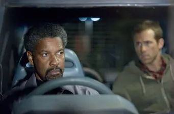 two men sit in car, driver looks serious, passenger glances away